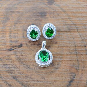 May include: A set of silver earrings and a pendant necklace with green gemstones surrounded by a halo of smaller white gemstones.