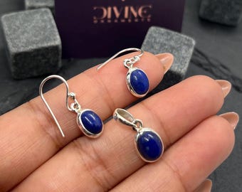 Puede incluir: Un conjunto de pendientes y un colgante de plata con piedras de lapislázuli ovaladas. Las piedras son de color azul intenso y están engastadas en plata.