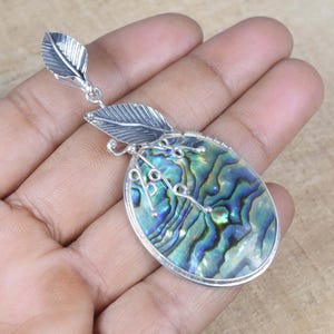 May include: A silver pendant with an oval abalone shell, displaying iridescent blue and green colours. The pendant has silver leaf details and a decorative wire design. The jewellery is designed to be worn as a necklace.