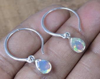 May include: A pair of silver hoop earrings with a teardrop-shaped opal gemstone dangling from each hoop.