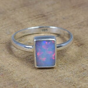 May include: A silver ring with a rectangular opal gemstone. The opal has a blue, pink, and white iridescent color.