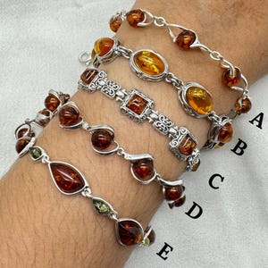 May include: Five silver bracelets with amber stones. The bracelets are stacked on a person's wrist. The bracelets are labeled A through E.