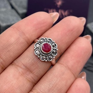 Può includere: Un anello d'argento con una pietra preziosa rossa incastonata in un design floreale.
