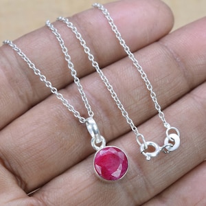 Peut inclure: Un collier en argent avec un pendentif rond orné d'une pierre précieuse rouge.