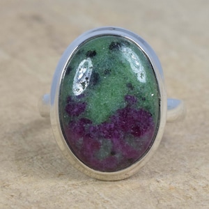 Puede incluir: Un anillo de plata con una piedra ovalada verde y morada. La piedra tiene un aspecto moteado con manchas negras.