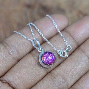 May include: A silver chain necklace with a round pendant featuring a purple iridescent glass stone.