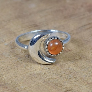 Puede incluir: Un anillo de plata con un diseño de media luna y una piedra de cornalina naranja.