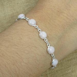 May include: A silver bracelet with pink opal stones. The bracelet has a delicate chain and is adorned with round, smooth stones.