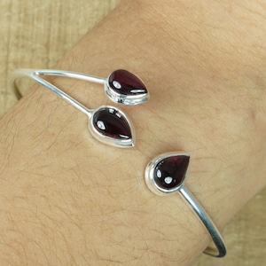 May include: A silver bangle bracelet with three teardrop-shaped red gemstones.