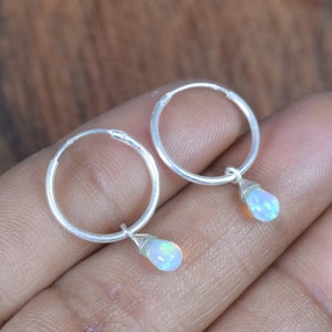 Könnte beinhalten: Ein Paar silberne Creolen mit einem kleinen, tropfenförmigen Opal, der an jeder Creole baumelt.