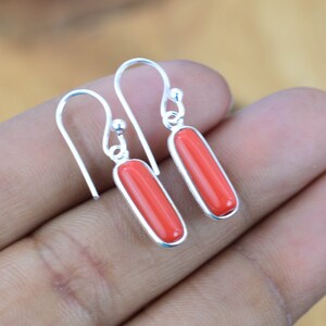 May include: A pair of silver dangle earrings with red coral stones. The stones are rectangular in shape and have a smooth, polished finish.