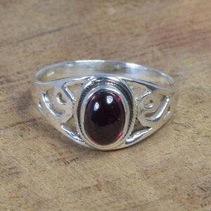 Peut inclure: Une bague en argent avec une pierre précieuse rouge foncé de forme ovale sertie dans un motif délicat et ajouré.