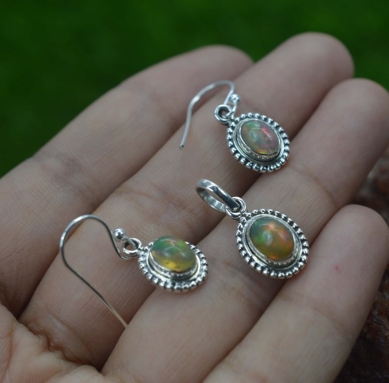 Puede incluir: Un conjunto de pendientes y un colgante de plata de ley con piedras preciosas de &oacute;palo de forma ovalada. Los pendientes tienen un dise&ntilde;o simple de gancho y el colgante tiene un aro para sujetarlo a una cadena.