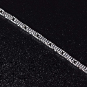 Può includere: Primo piano di una catena d'argento con un design a maglie quadrate. La catena è angolata su uno sfondo nero. Le maglie sono rettangolari e hanno una superficie strutturata.