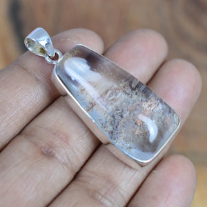 May include: A silver pendant featuring a clear quartz crystal with inclusions of grey and brown. The crystal is set in a silver bezel and has a rectangular shape.