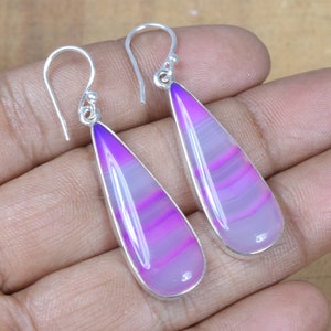 May include: A pair of silver dangle earrings featuring purple and white agate stones. The stones are teardrop shaped and have a striped pattern.