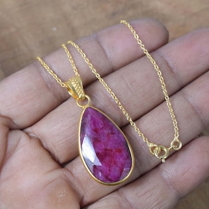 Puede incluir: Un collar de cadena de oro con un colgante en forma de lágrima con una piedra de rubí rojo oscuro.