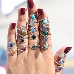 May include: A hand model wearing a variety of silver rings with different coloured gemstones. The rings are all designed with a twisted band.