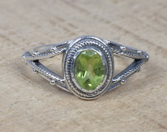 May include: A silver ring with an oval-shaped green peridot gemstone set in a delicate filigree design.