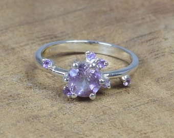 May include: A silver ring with a large, round, purple amethyst gemstone surrounded by smaller amethyst stones.