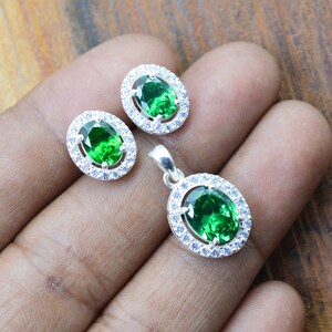 May include: A silver pendant necklace and earrings set with a large oval green gemstone surrounded by smaller white gemstones.