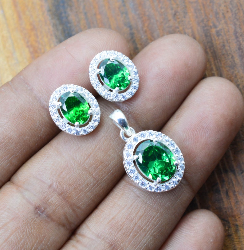 May include: A silver pendant necklace and earrings set with a large oval green gemstone surrounded by smaller white gemstones.