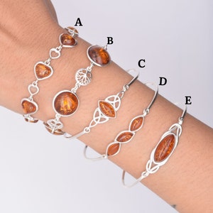 May include: Five silver bracelets with amber stones. The bracelets feature different designs, including hearts, Celtic knots, and leaves.