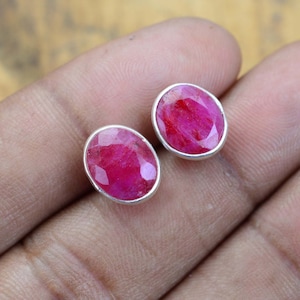 May include: A pair of oval-shaped ruby earrings set in sterling silver. The rubies are a deep pink colour and have a faceted cut.