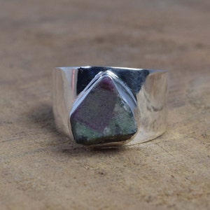 May include: A silver ring featuring a large, faceted, green, pink, and grey gemstone set in the centre.