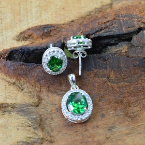 May include: A set of silver earrings and a pendant necklace with green oval gemstones surrounded by a halo of smaller white gemstones.