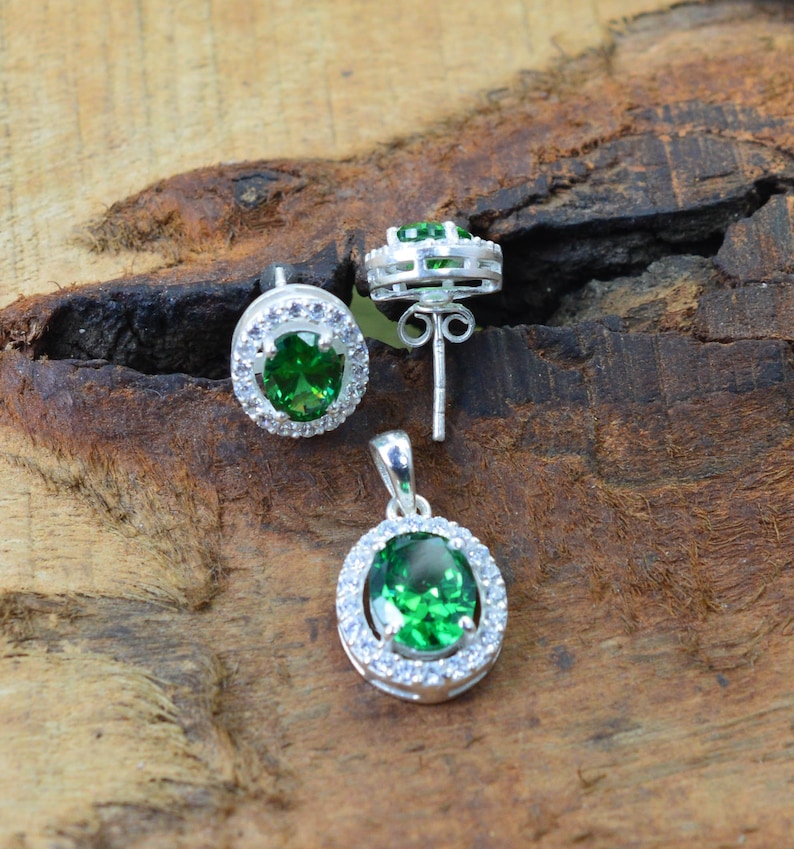May include: A set of silver earrings and a pendant necklace with green oval gemstones surrounded by a halo of smaller white gemstones.
