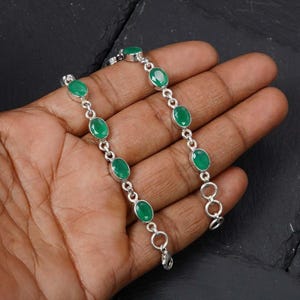 May include: A silver chain bracelet featuring a series of oval-shaped, faceted green gemstones set in individual metal bezels. The bracelet is constructed with circular silver links connecting each stone, finished with a small metal lobster claw clasp.