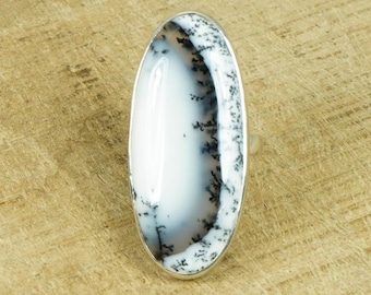 May include: A silver ring with a large oval dendritic agate stone. The stone is white with black dendritic patterns.