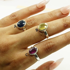 Puede incluir: Tres anillos de plata con piedras preciosas de forma ovalada. El anillo etiquetado como 'A' tiene una piedra preciosa azul oscuro, el anillo etiquetado como 'B' tiene una piedra preciosa amarilla clara y el anillo etiquetado como 'C' tiene una piedra preciosa roja oscura.