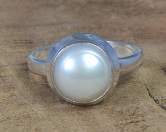 Puede incluir: Un anillo de plata con una perla blanca engastada en un bisel redondo.