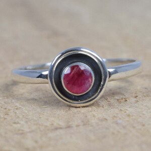 May include: A silver ring with a red gemstone set in a black and silver bezel.