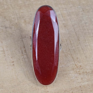 May include: A silver ring featuring a large, oval-shaped, red gemstone.