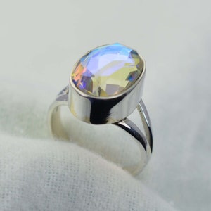May include: A silver ring featuring a large oval-shaped iridescent gemstone. The gemstone has a pale yellow base with blue and purple tones.