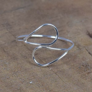Op de afbeelding: Een zilveren ring met een dubbel traanontwerp. De ring is gemaakt van dunne draad en is delicaat van uiterlijk.