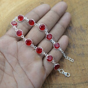 May include: A silver bracelet with red gemstone beads. The bracelet has a lobster clasp closure.