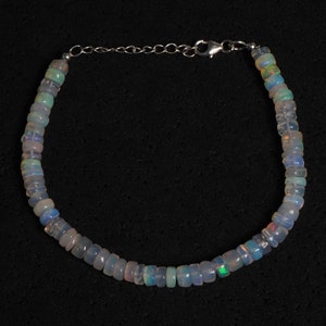 May include: A silver chain bracelet with iridescent white opal beads. The bracelet is made of small, square-shaped beads.