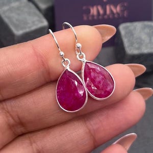 Op de afbeelding: Een paar zilveren oorhangers met druppelvormige roze robijnen.