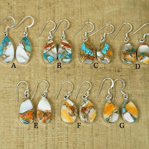 以下が含まれることがあります： ターコイズ、オレンジ、ホワイトのミックスカラーの涙型ストーンが特徴の、7ペアのドロップイヤリングのセット。イヤリングはAからGまでラベル付けされています。
