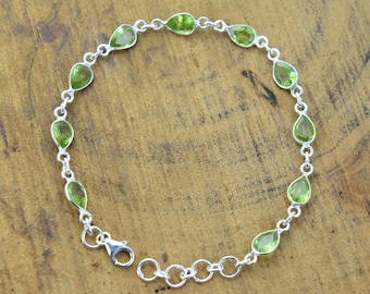 Op de afbeelding: Een zilveren kettingarmband met groene peervormige edelstenen. De armband heeft een karabijn sluiting.