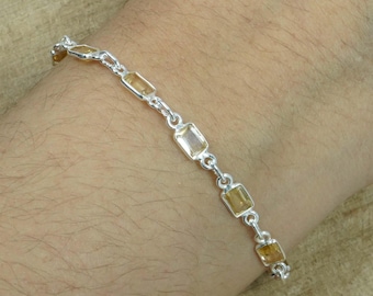 Könnte beinhalten: Ein silbernes Armband mit rechteckigen, hellgelben Edelsteinen. Das Armband besteht aus kleinen, verbundenen Silbersegmenten, die jeweils einen Edelstein halten. Die Edelsteine sind gleichmäßig verteilt.