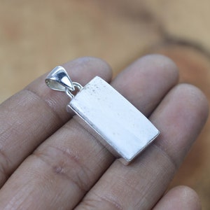 May include: A white rectangular pendant with a silver bail. The pendant is made of a smooth, polished material.