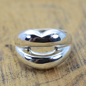 May include: A silver ring shaped like a pair of lips. The ring is smooth and shiny.
