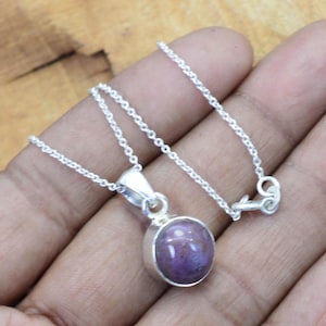 May include: A silver necklace featuring a round, purple pendant. The pendant has a polished surface and is set in a silver bezel. The chain is delicate and has a simple clasp.