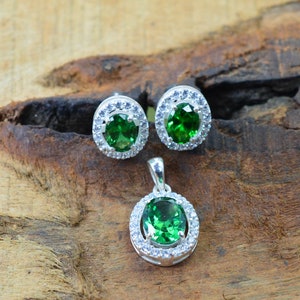 May include: A silver pendant and earrings set with a green gemstone surrounded by a halo of smaller white gemstones.