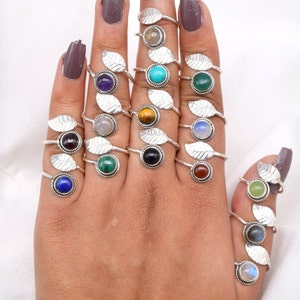 Könnte beinhalten: Ein Set mit 14 Silberringen mit verschiedenen farbigen Edelsteinen, die in blattartigen Designs gefasst sind. Die Ringe werden an einer Hand getragen, wobei jeder Finger mit mehreren Ringen geschmückt ist.